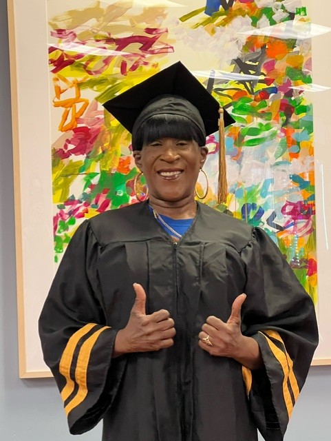 Tracey Downing posing in her graduation gown with two thumbs up