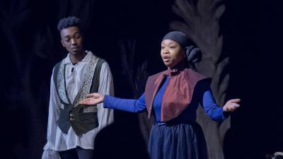 Actor speaks with outstretched arms while another actor looks on.