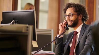 A paralegal looks at his computer while on the phone with a client.