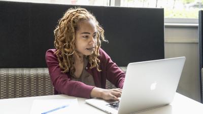 Student studying alone at a laptop with pen and paper on the table.