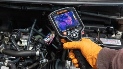 Hand holds diagnostic tool over car engine.