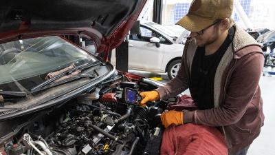 Student uses diagnostic tool over car engine.