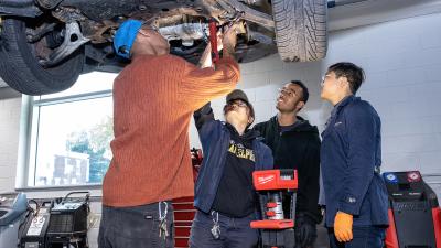 Four students work under a truck on a lift.