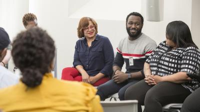 Group sitting in a circle react with smiles to person speaking.