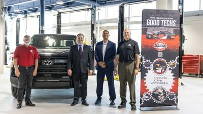 A group stands in a modern automotive garage in front of a truck and next to a banner.
