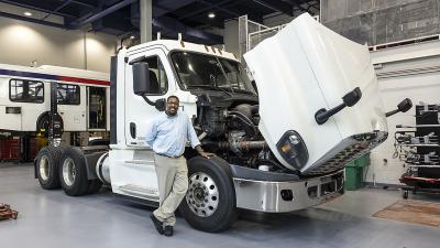 Instructor poses with tractor trail truck hood open to show engine.