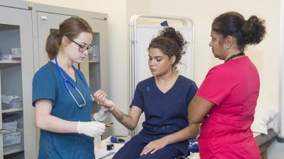 Instructor observes a student practicing taking a pulse on another student.