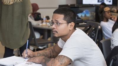 Student holding a pen looks up from his open book.