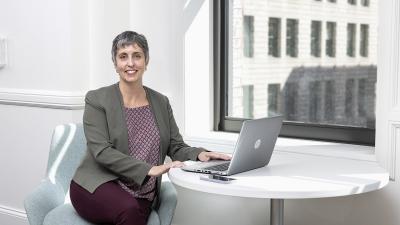 Business woman seated at a table with a laptop smiles for the camera.