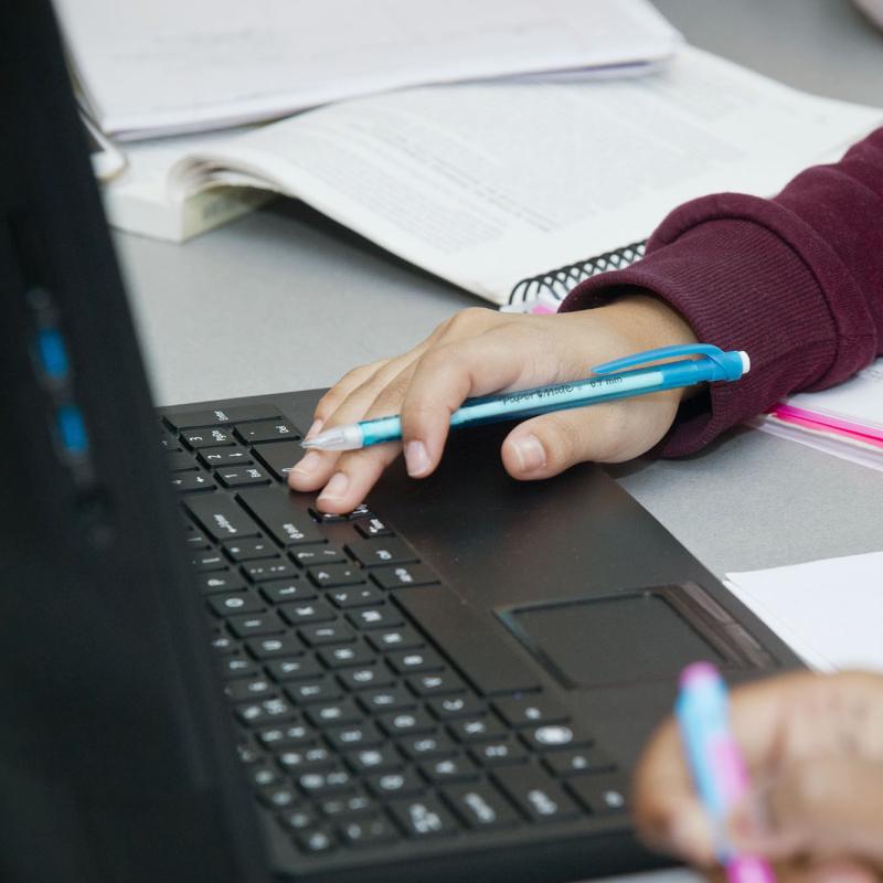 Arm holding pen at computer laptop keyboard.