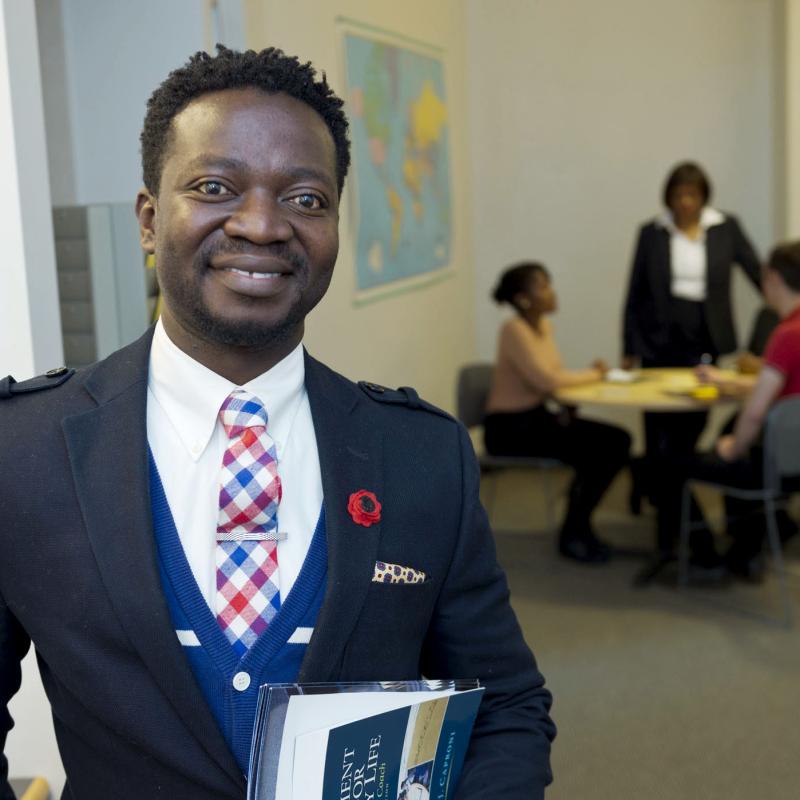 Gentleman holding books smiles for the camera while a group works in the background.