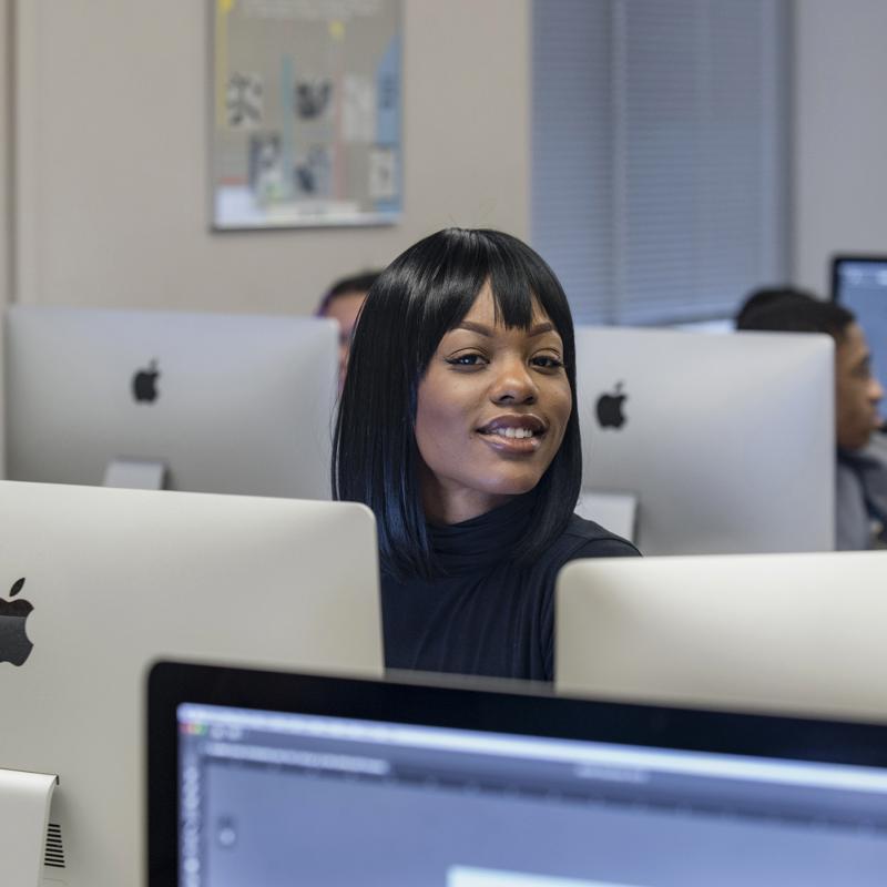 Woman amongst computer screens smiles for the camera.