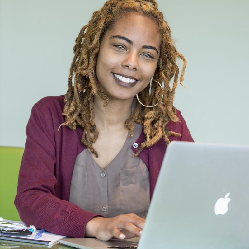 Woman working on laptop smiles for the camera.