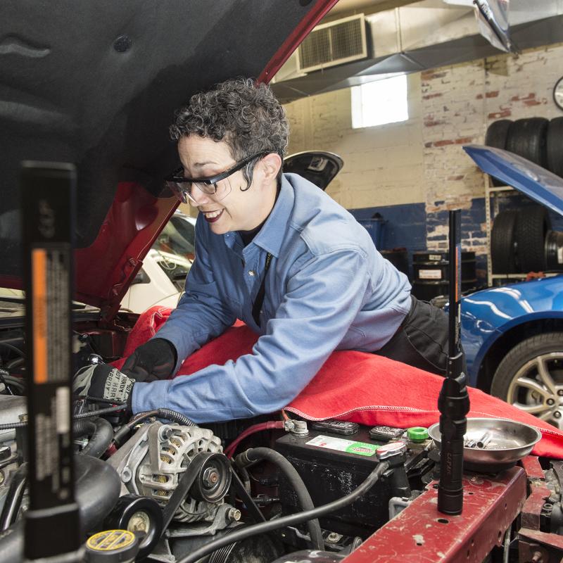 Woman works under the hood of an automobile.