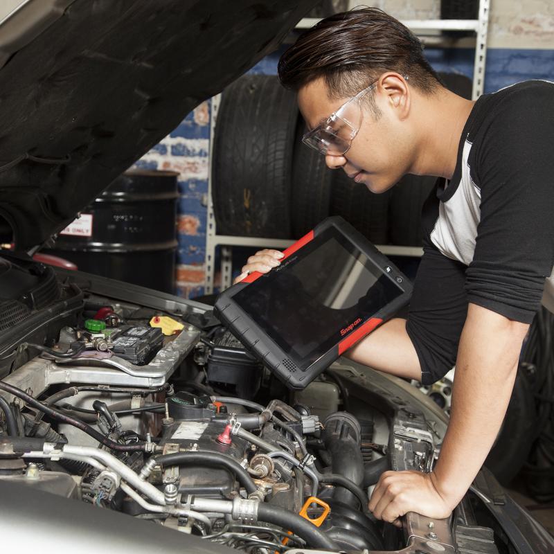 Automechanic leans over car engine with diagnostic tool.