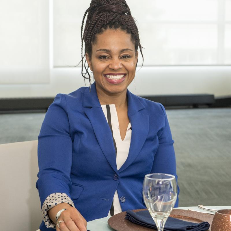 Woman in business attire sits at set dinner table.