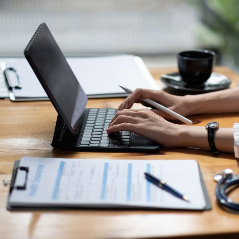 Hands type on laptop with charts on desk.