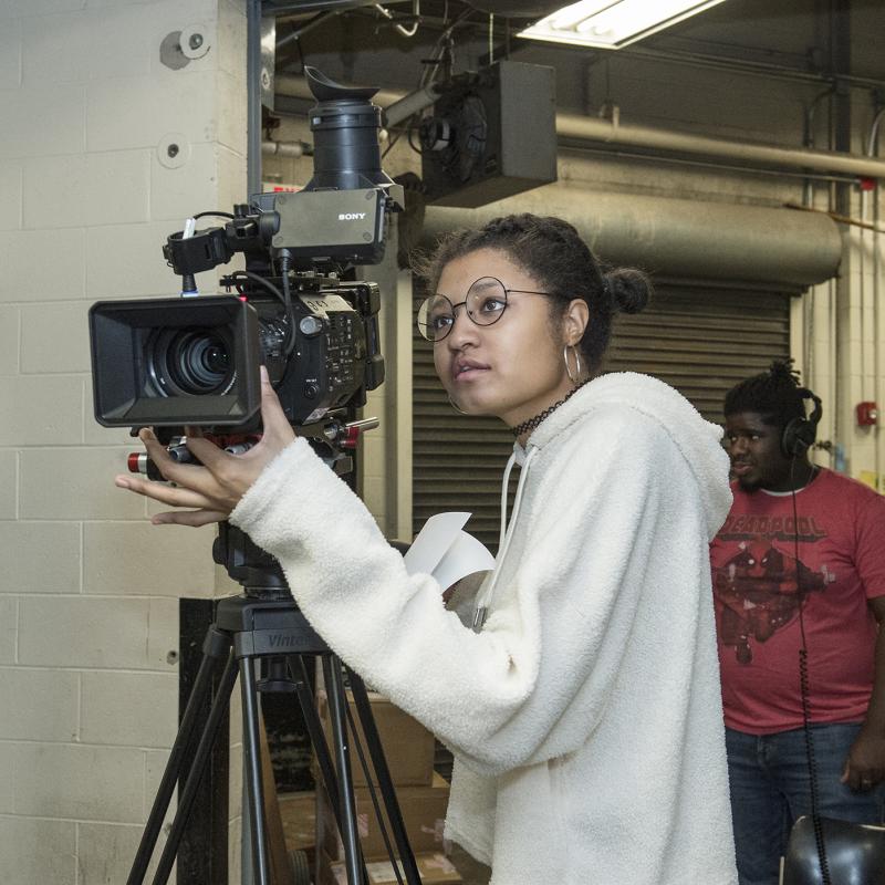 A woman focuses a video camera.