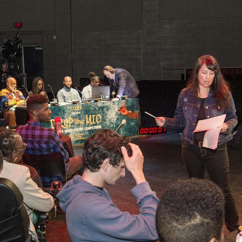 Woman with script speaks with performers on stage.
