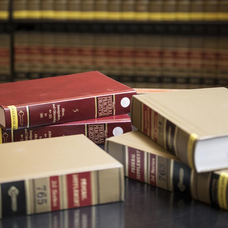 Law books piled on desk with shelves of law books in the background.