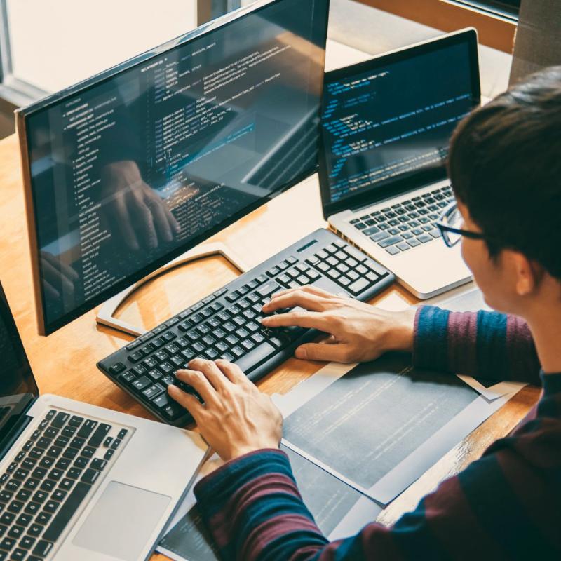 Man sits at three computers working on central computer.