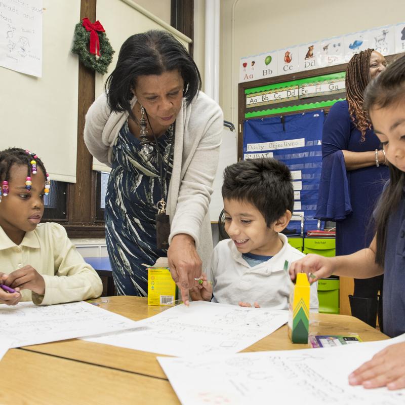 A teacher leans over a table of students coloring.