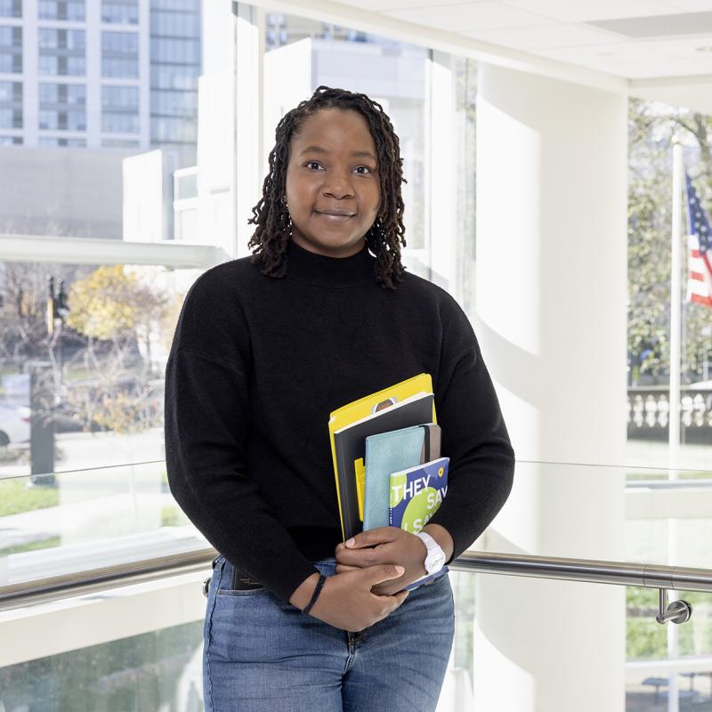 Woman stands holding school books.