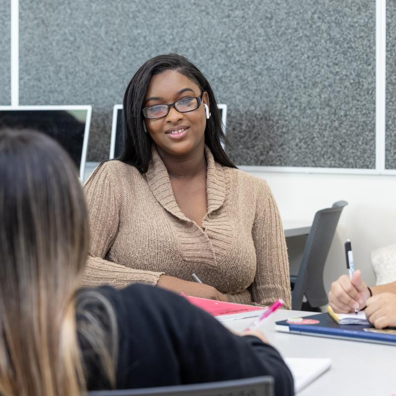 Woman at a table with others smiles for the camera.