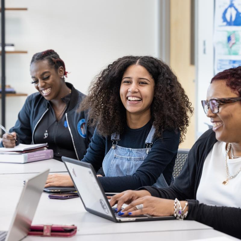 Students in a classroom laugh as they work.