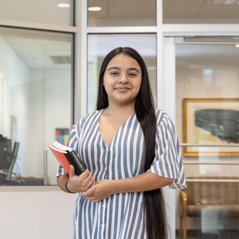 Woman holding books in an office setting smiles for the camera.