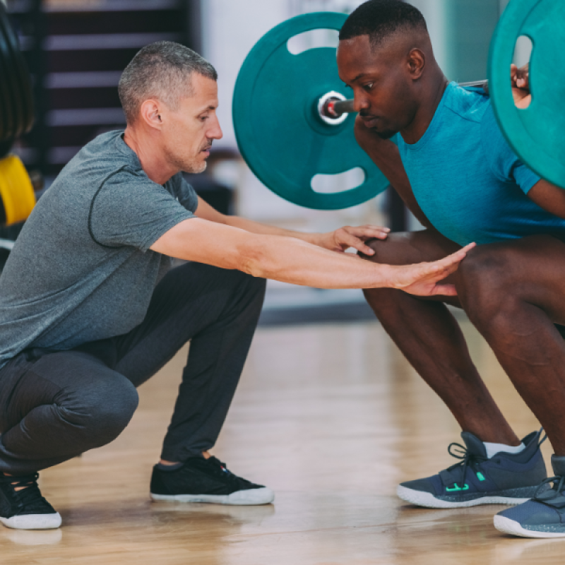 Trainer helping client do a squat with a big barbell