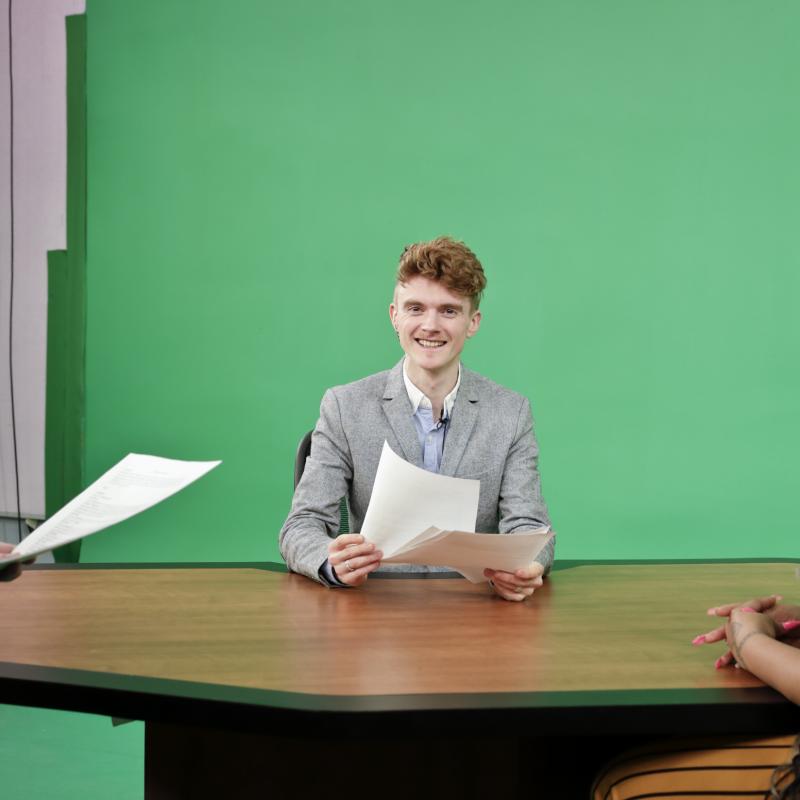 Student in front of a greenscreen at a news desk who is a tv journalist at CCPTV