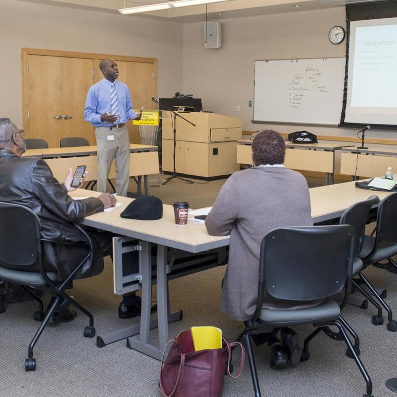 A man standing at the front of a meeting room presenting to a group of people facing him