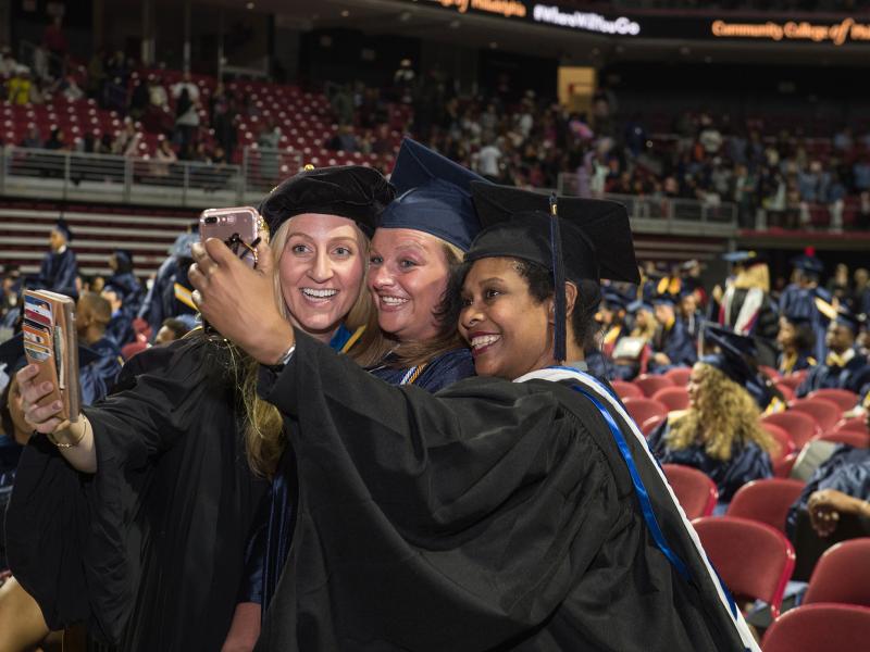 students at graduation taking a selfie with a professor