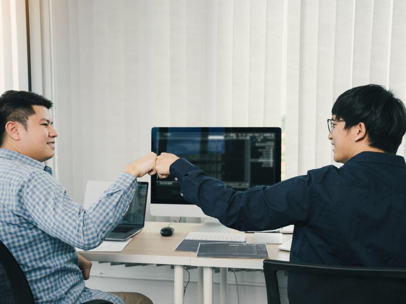 Two people smiling and fist bumping while coding together