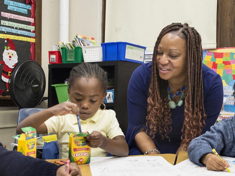 A grade school teacher watches their students color.