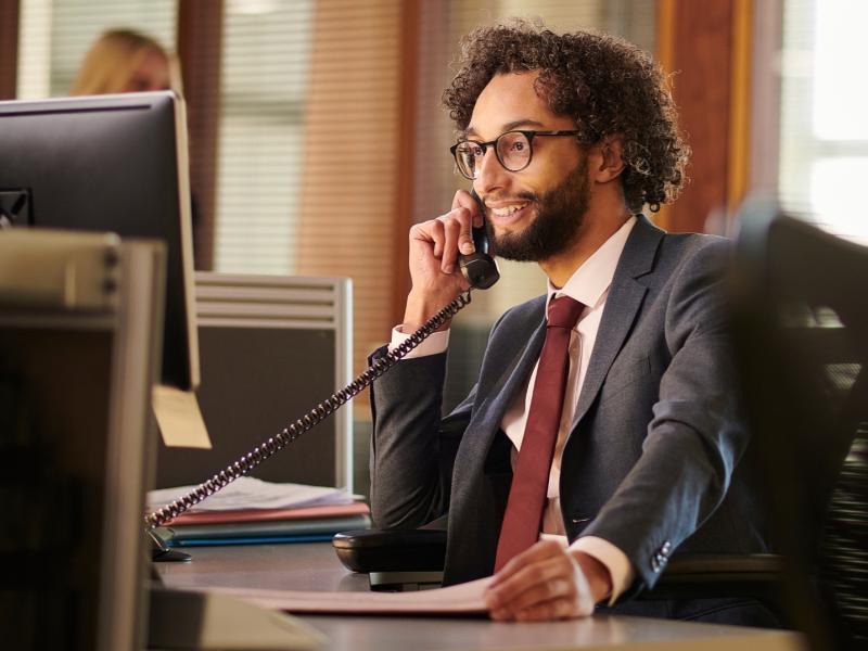 A paralegal looks at his computer while on the phone with a client.