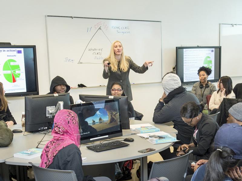 Instructor talks to crowded classroom in front of a board with a diagram drawn on it.
