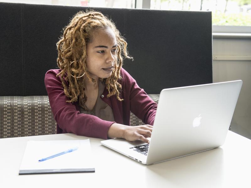 Student studying alone at a laptop with pen and paper on the table.