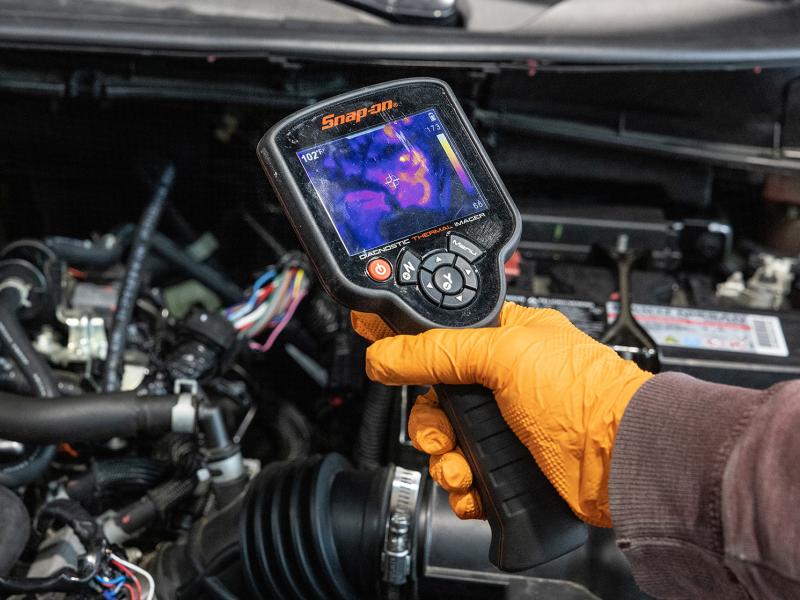 Hand holds diagnostic tool over car engine.