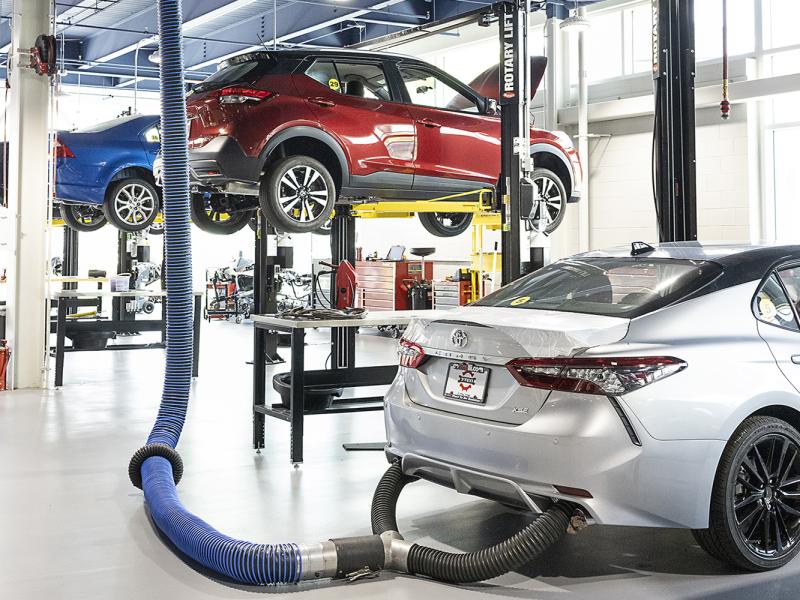 Large modern automotive garage with three cars and various tools.