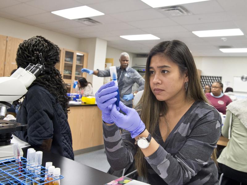 Student examines test tube while instructor speaks to the class in the background.