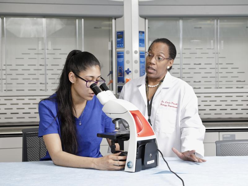 Instructor teaches a student how to use a microscope.