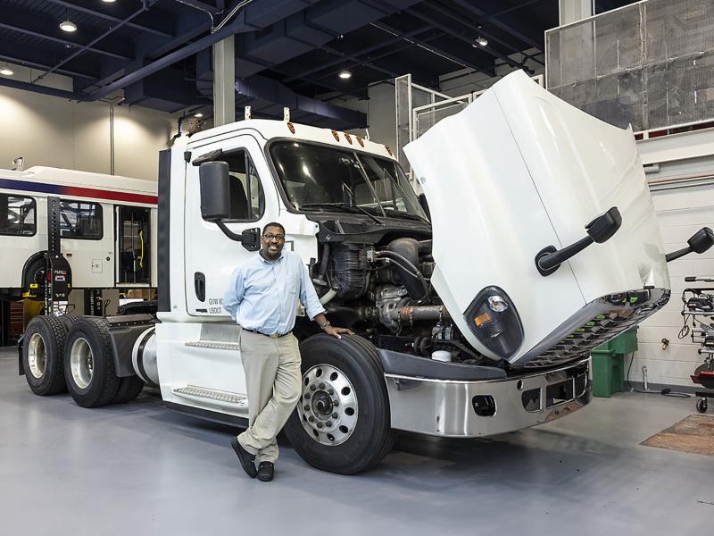 Instructor poses with tractor trail truck hood open to show engine.