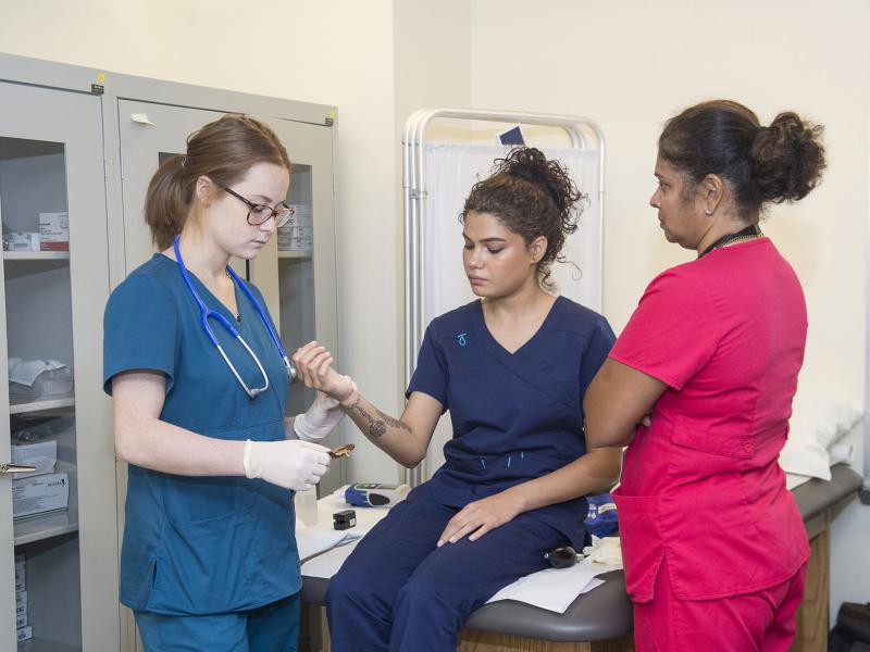 Instructor observes a student practicing taking a pulse on another student.