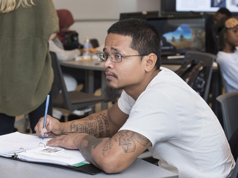 Student holding a pen looks up from his open book.