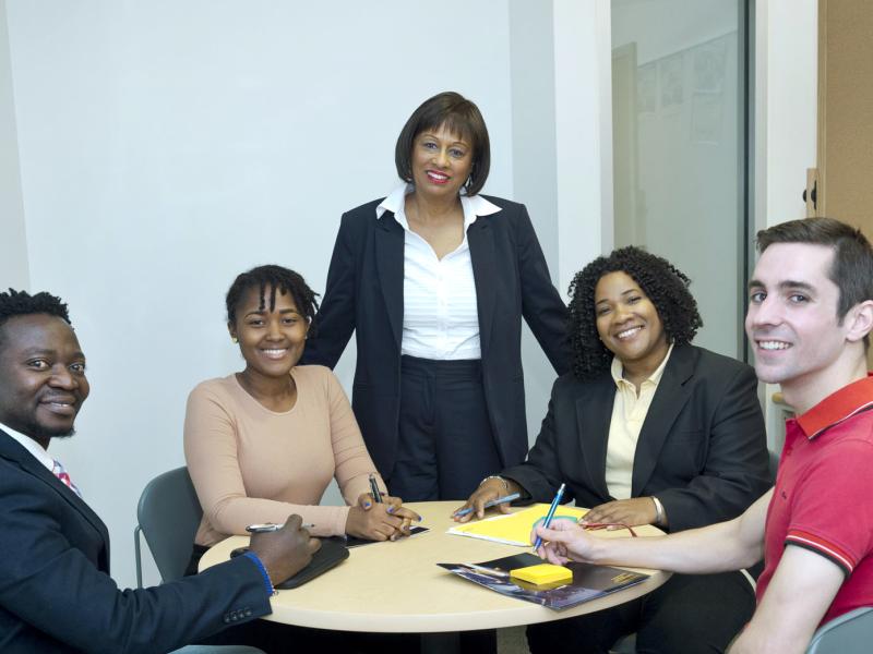 A group of five people in business attire, gathered around a table, smile for the camera.