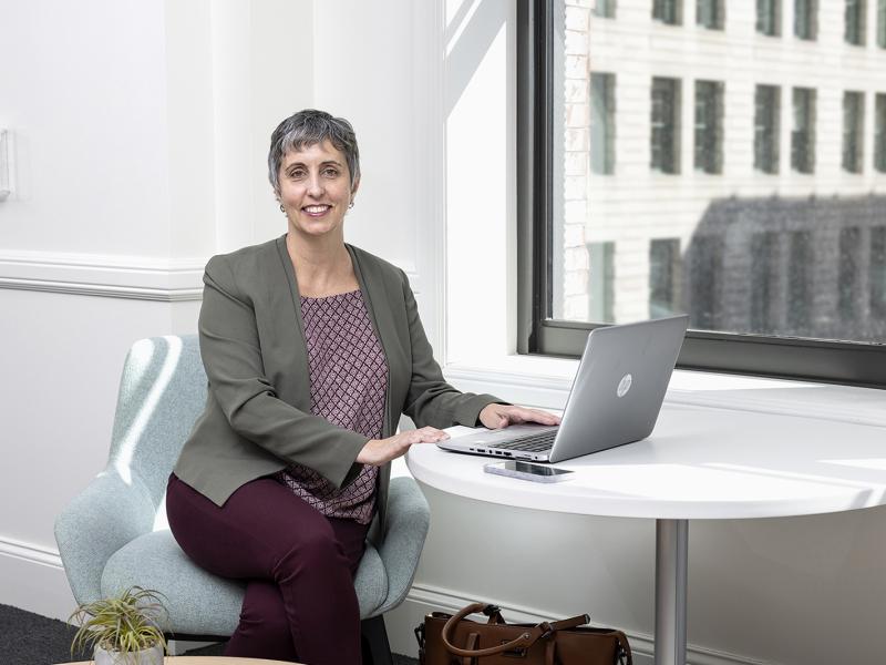 Business woman seated at a table with a laptop smiles for the camera.