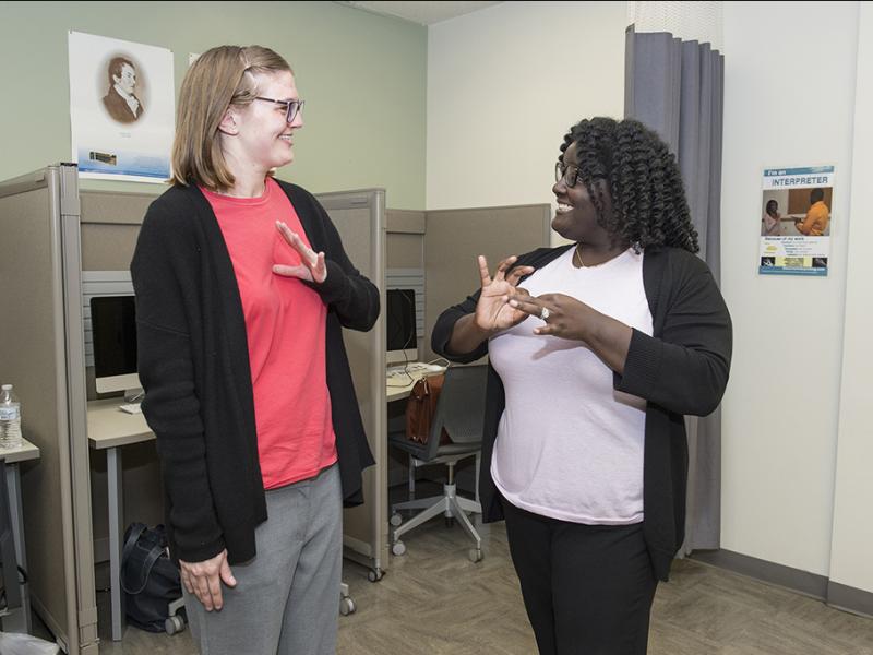 two students smiling and communicating in American Sign Language (ASL)