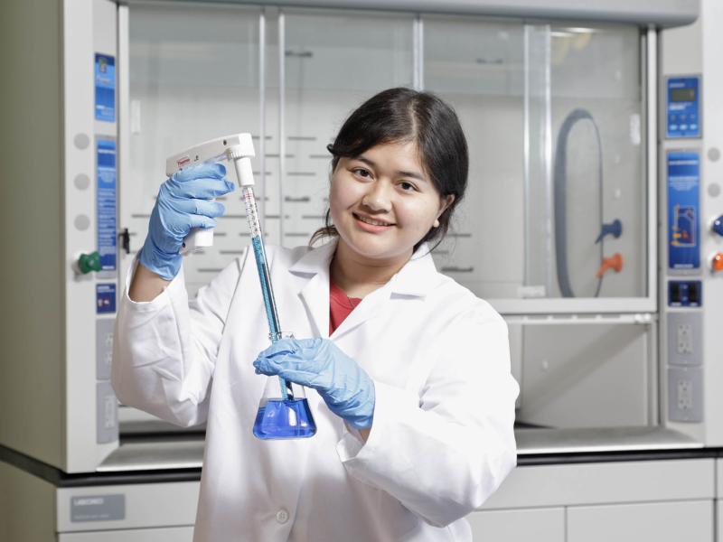 smiling student wearing a lab coat working in the biology lab